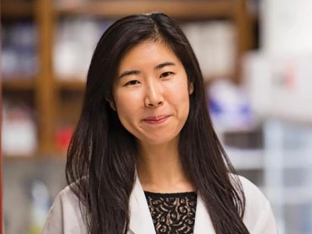 Woman in a lab coat standing in a laboratory, smiling slightly.