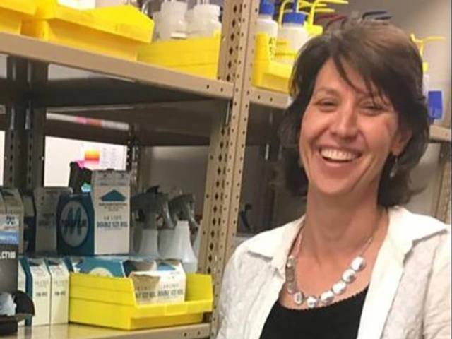 Jennifer Katcher smiling in a science lab, standing in front of lab supplies and shelves.