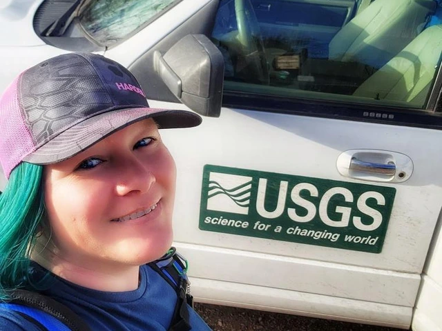 Woman with teal hair smiling in front of a white USGS vehicle with 'science for a changing world' logo