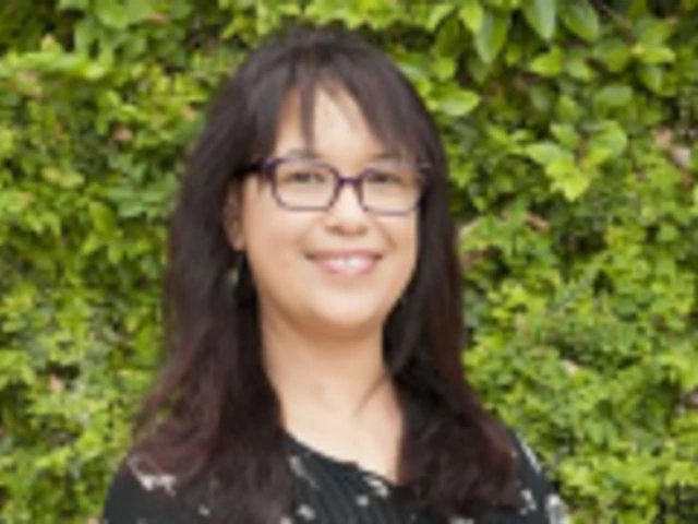 Woman with glasses smiling in front of leafy green background