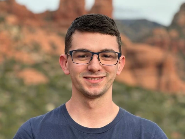 Young man wearing glasses and a 'This is what a UA Engineer student looks like' t-shirt, smiling with red rock formations in the background