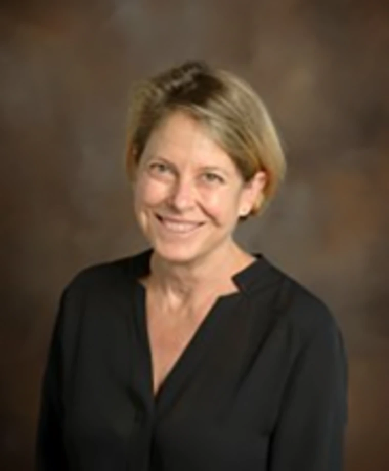 Studio portrait of Dr. Michele Walsh wearing a black blouse, smiling in front of a brown gradient background.