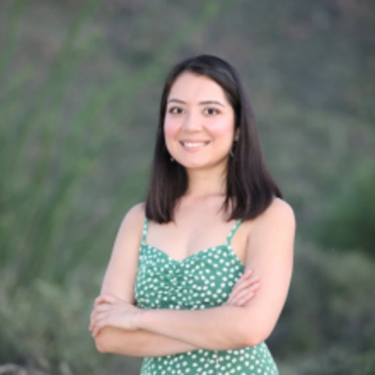 Outdoor portrait of Elia Bueno wearing a green polka dot dress, smiling with arms crossed in front of a desert landscape.