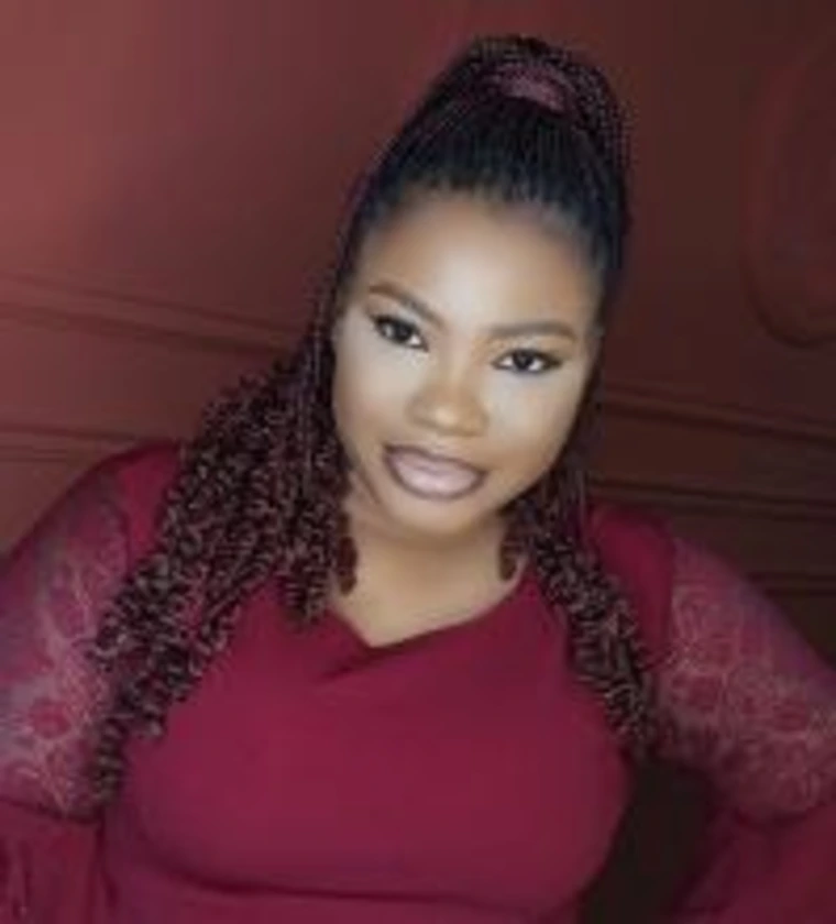 Headshot of Adenike Samuel in a maroon top with lace sleeves, wearing braids and smiling slightly against a deep red background.