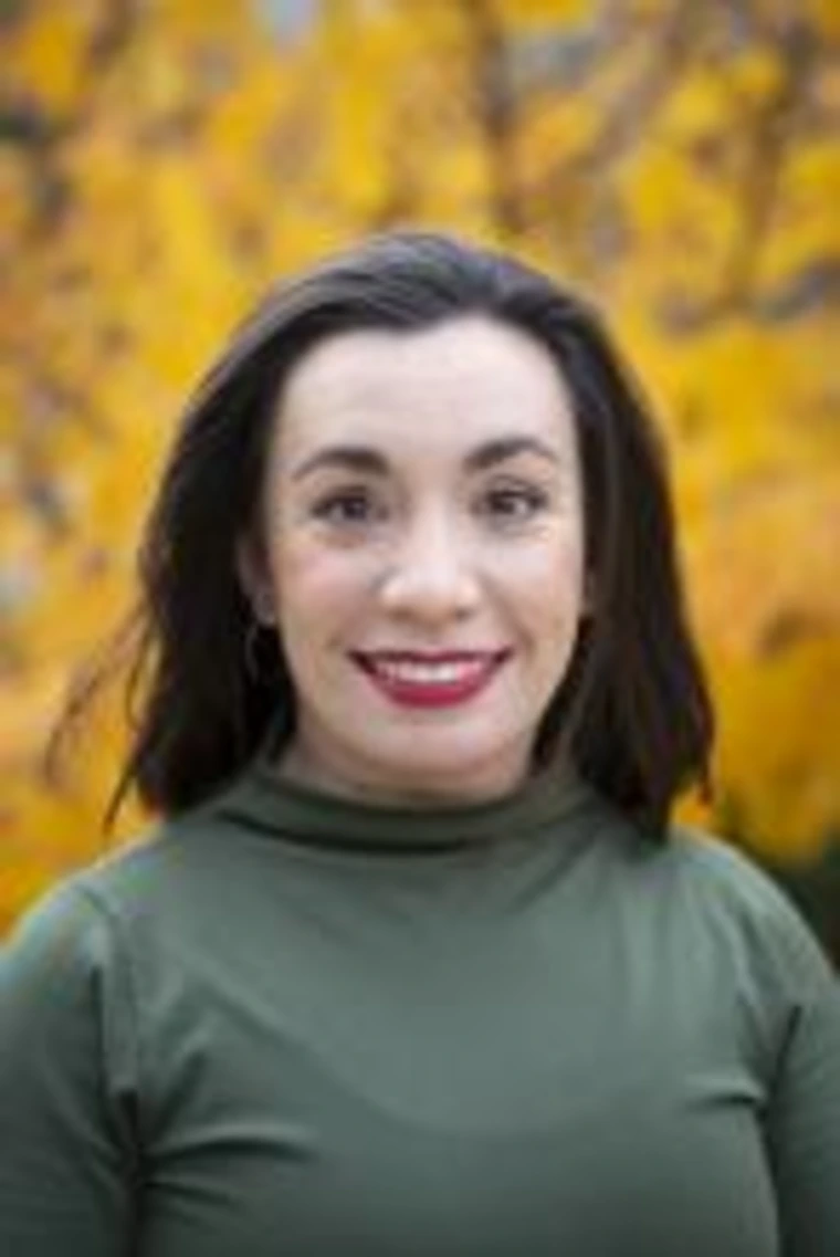 Headshot of Patricia Olivas smiling in front of a tree with vibrant yellow leaves, wearing a green turtleneck top.