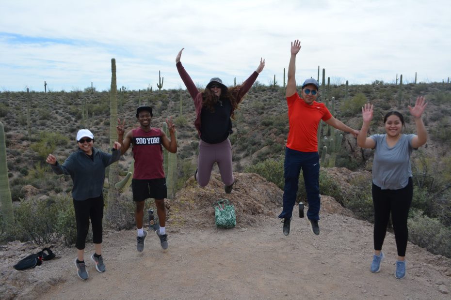 five young individuals jumping in the desert under a sunny sky