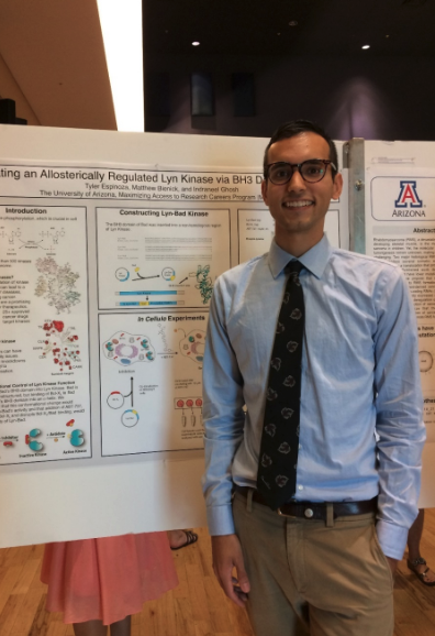 young man with blue shirt, tie, khaki pants standing in front of a presentation board