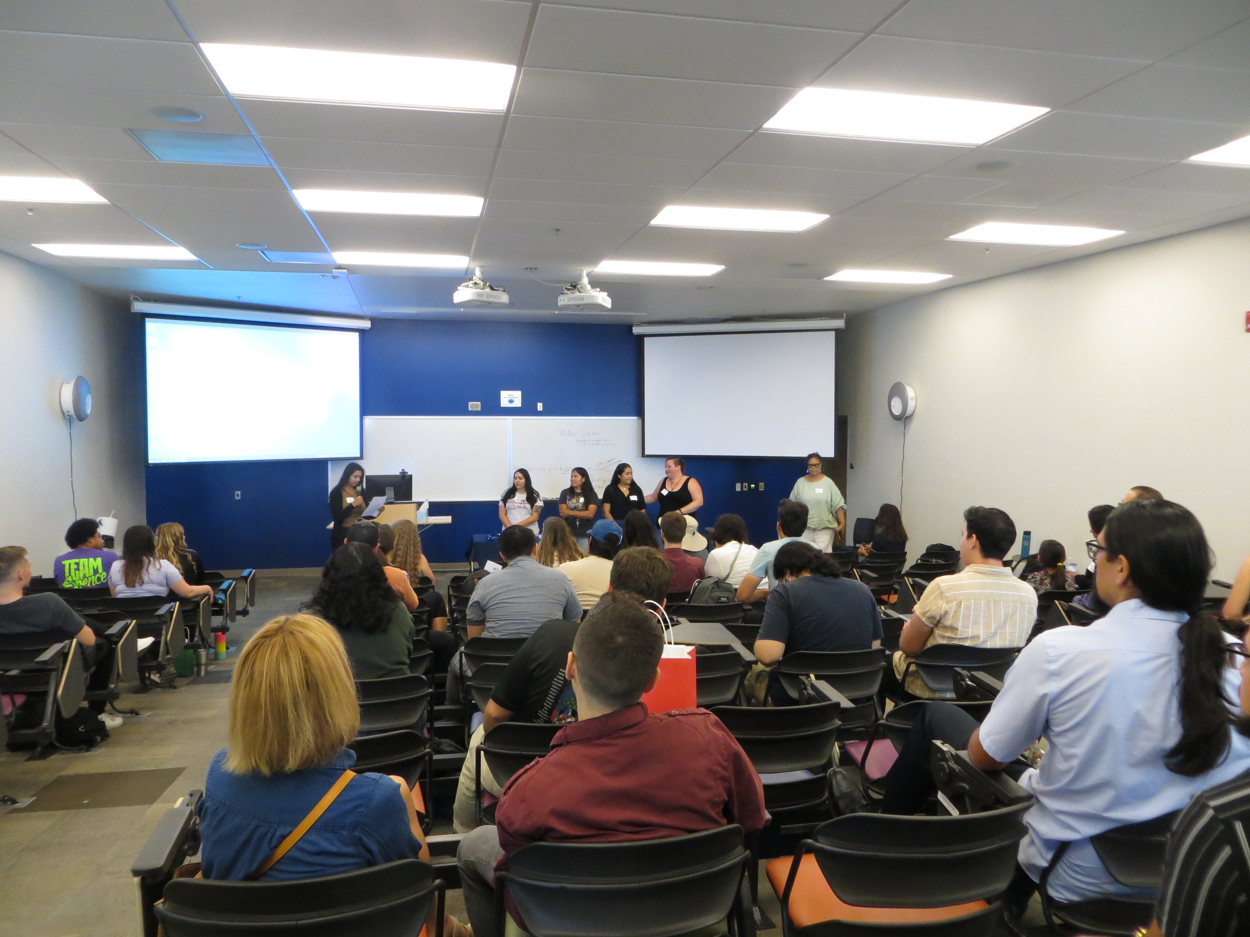 a large gathering of students in a conference room, listening to a speaker